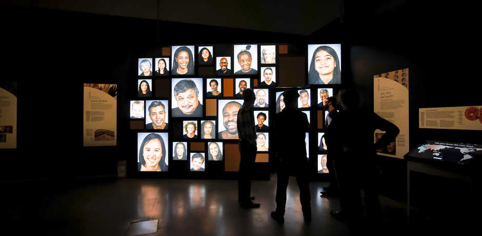 Video portrait wall from the Academy's Skin exhibit, with silhouetted guests in foreground