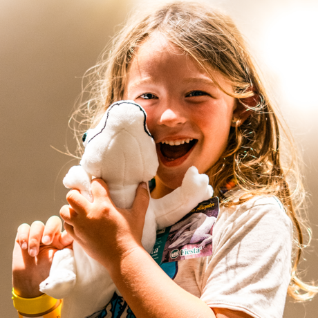 Child holding plush animal of Claude the alligator with albinism